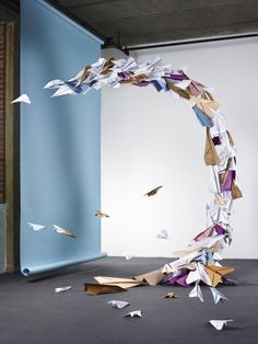 paper birds are flying in the air near a blue wall and an arch made out of origami