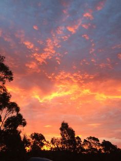 the sun is setting behind some trees and clouds in the sky, with one car parked on the side of the road