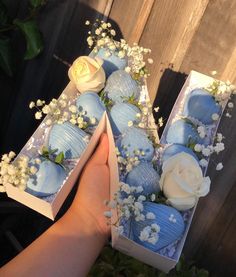 someone is holding two boxes with blue and white cakes in them, one has a rose on it