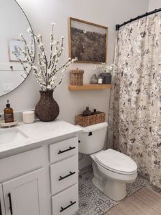 a white toilet sitting next to a sink in a bathroom under a mirror with flowers on it