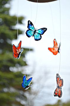 several butterflies are hanging from a string in the air, with trees in the background