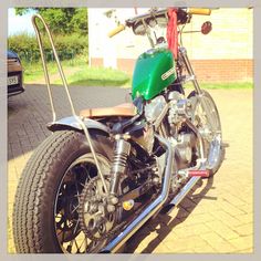 a green motorcycle parked on top of a brick road next to a car and another vehicle