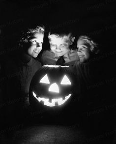 black and white photograph of three children in front of a jack - o - lantern