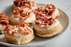 four donuts with bacon on them are sitting on a white plate and have been topped with icing