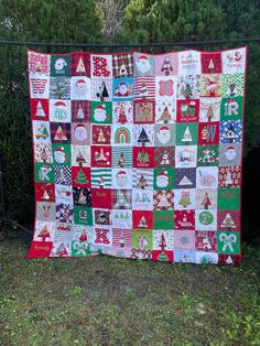 a quilted christmas tree is hanging on a fence in front of some trees and bushes