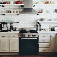 a stove top oven sitting inside of a kitchen next to white cupboards and shelves