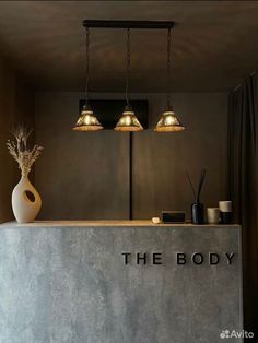 the body is sitting on top of a counter with three lights above it and two vases behind it