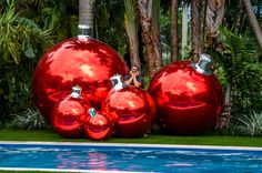 three shiny red christmas balls sitting next to a swimming pool with palm trees in the background