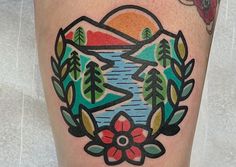 a colorful tattoo on the leg of a woman with trees and mountains in the background