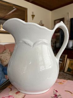 a white pitcher sitting on top of a table next to a pink flowered cloth