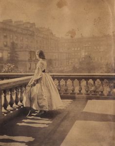 an old photo of a woman in a long dress standing on a balcony overlooking the city