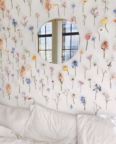 a bedroom with flowers on the wall and a round mirror above it's bed