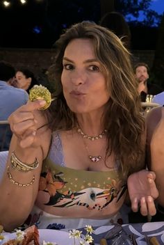 a woman sitting at a table with food in her hand and looking up to the camera