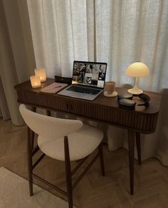 a laptop computer sitting on top of a wooden desk next to a lamp and chair