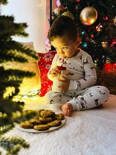 a baby sitting in front of a christmas tree eating cookies