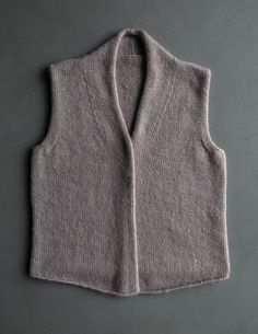 a gray sweater vest sitting on top of a grey table next to a white wall