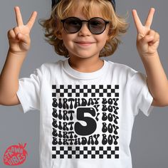 a young boy wearing sunglasses and a hat making the peace sign with his hands while standing in front of a gray background