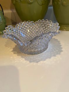 a glass bowl sitting on top of a table next to two green vases in the background