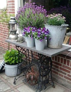 several potted plants are sitting on an old sewing machine and some books in front of a brick building