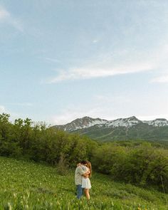 a man and woman standing in the middle of a lush green field with mountains in the background