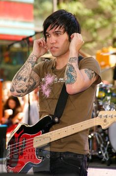 a man with tattoos on his arms and shoulder holding a guitar in front of him