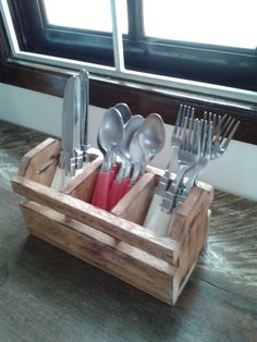 a wooden box with utensils in it on a table next to a window