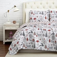 a bed with a christmas themed comforter and pillows on top of it in front of a white brick wall