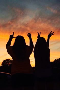 two girls are silhouetted against an orange and blue sky with their hands in the air