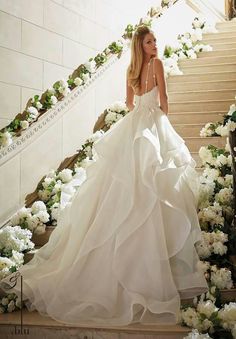 a woman in a wedding dress walking down some stairs with flowers on the side and behind her