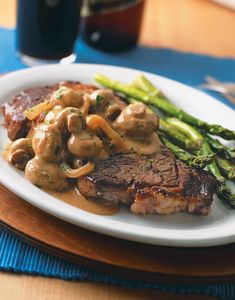 steak with mushrooms and asparagus on a plate next to a glass of beer