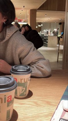 a woman sitting at a table with two coffee cups in front of her and another cup next to her