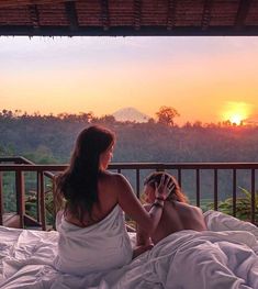 two women sitting on a bed looking at the sunset