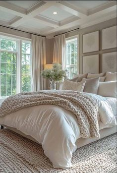 a large white bed sitting in a bedroom next to two windows and a rug on the floor