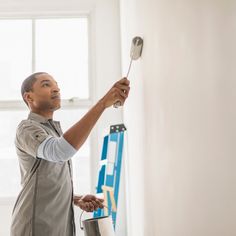 a man holding a paint roller in his right hand and painting on the wall behind him