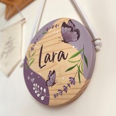 a wooden sign hanging from the side of a wall with butterflies painted on it's sides