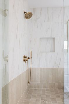 a bathroom with marble walls and tile flooring, shower head and hand shower faucet