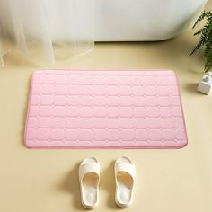 a pair of white slippers sitting on top of a pink mat next to a potted plant