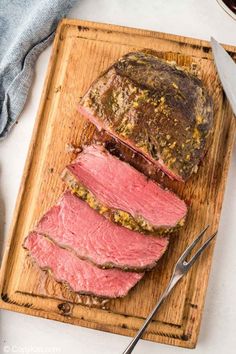 sliced roast beef on a cutting board with knife and fork