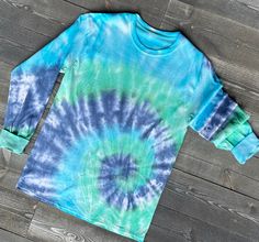 Dreaming of the beach or lake day ... cozy up in the SUBTLE WAVES, this tie-dye will set the mood for a day on the water. The originally white t-shirt is spiral dyed with hues of blue, green and turquoise. It's a long sleeve or short sleeve 100% cotton t-shirt that is super comfy and pairs well with shorts, leggings, or jeans. Each shirt is made to order a unique. SIZING: Runs true to size for most. COLOR: Originally white, the shirt is now tie-dyed with shades of blue, green, and turquoise. No Lake Day, Green And Turquoise, How To Tie Dye, Tie Dye Outfits, Color Swirl, Tie Dye Long Sleeve, Tie Dye Sweatshirt, Tie Dye Hoodie, Tie Dye Shirt