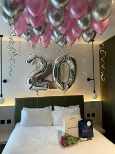 balloons are hanging from the ceiling above a bed with white linens and pink and silver decorations