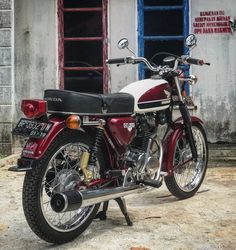 a red and white motorcycle parked in front of a building with blue shuttered windows