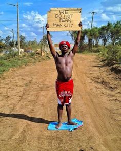 a man holding up a sign in the middle of a dirt road