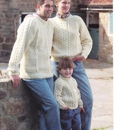 two adults and a child standing next to each other in front of a stone wall