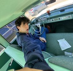 a man sitting in the driver's seat of an old car with his hand on the steering wheel