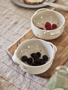 two white bowls filled with raspberries on top of a wooden cutting board