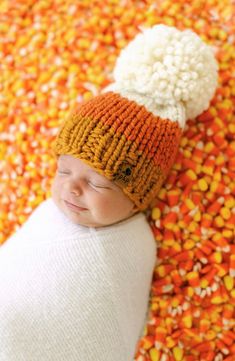 a baby wearing a knitted orange and white hat laying on top of corn kernels