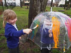 two young children standing in the rain holding an umbrella and brush with paint on it