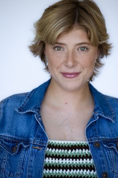 a woman with short hair wearing a jean jacket and striped shirt smiling at the camera