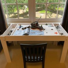 a table with many items on it in front of a window and a chair next to it