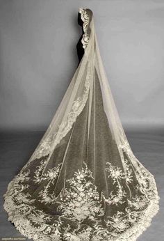 the back of a wedding veil with flowers and leaves on it, against a gray background